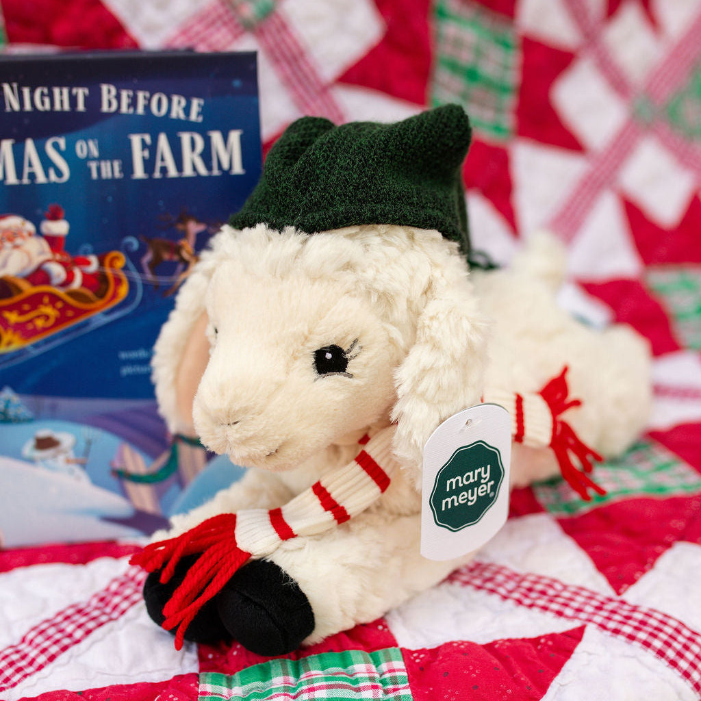 Plush lamb toy with green hat and red scarf on a quilted background