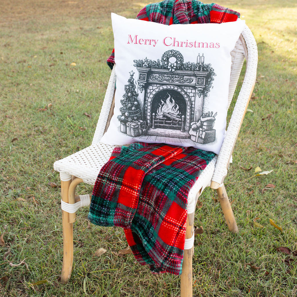 Chair with a 'Merry Christmas' pillow and plaid blanket in a grassy outdoor setting.