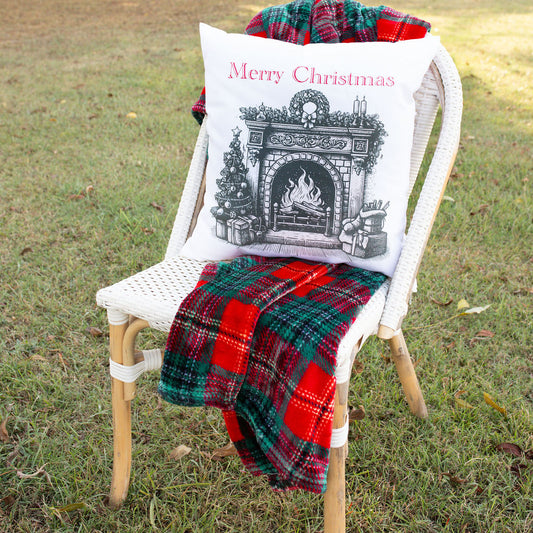 Chair with a 'Merry Christmas' pillow and plaid blanket in a grassy outdoor setting.
